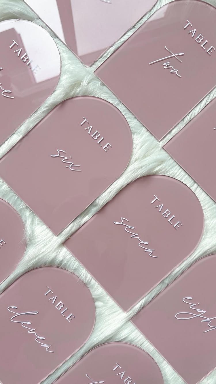 Dusty rose arched acrylic table number signs resting on white faux fur fabric.