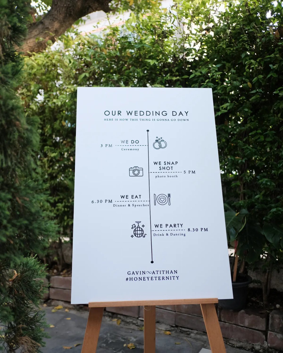 Wedding timeline sign on a wooden easel detailing the schedule of events outdoors.