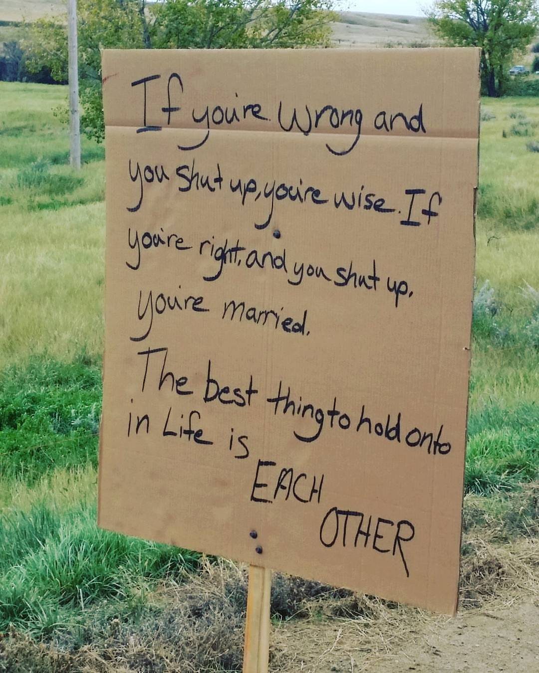 Handwritten cardboard wedding sign with funny marriage advice in a grassy field