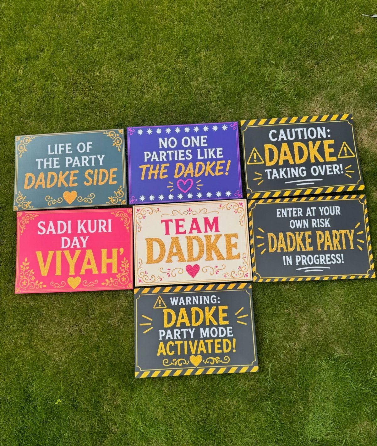 Colorful humorous wedding signs with text about Dadke party laid on green grass.