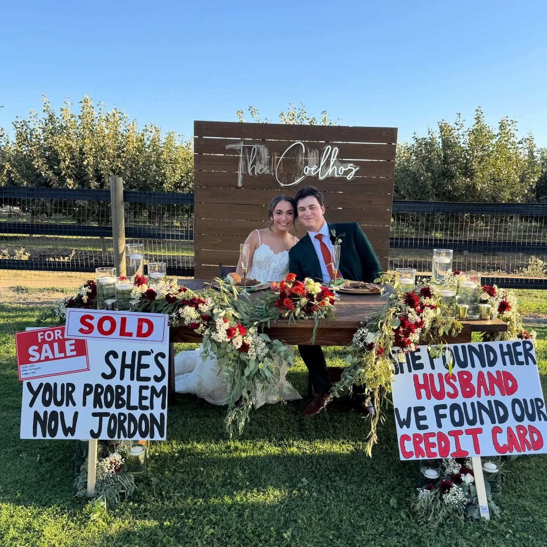 Bride and groom sitting behind funny wedding signs on a grassy lawn