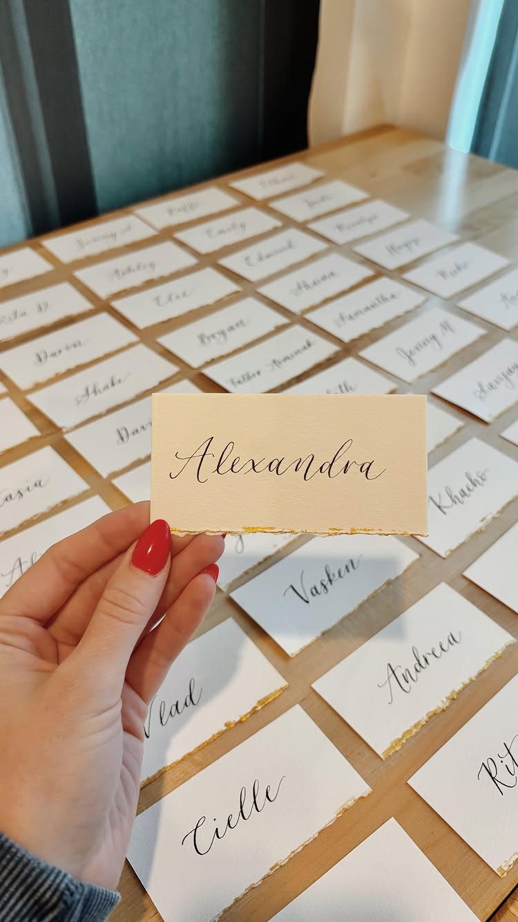 Hand holding a gold calligraphy place card among many others on a table