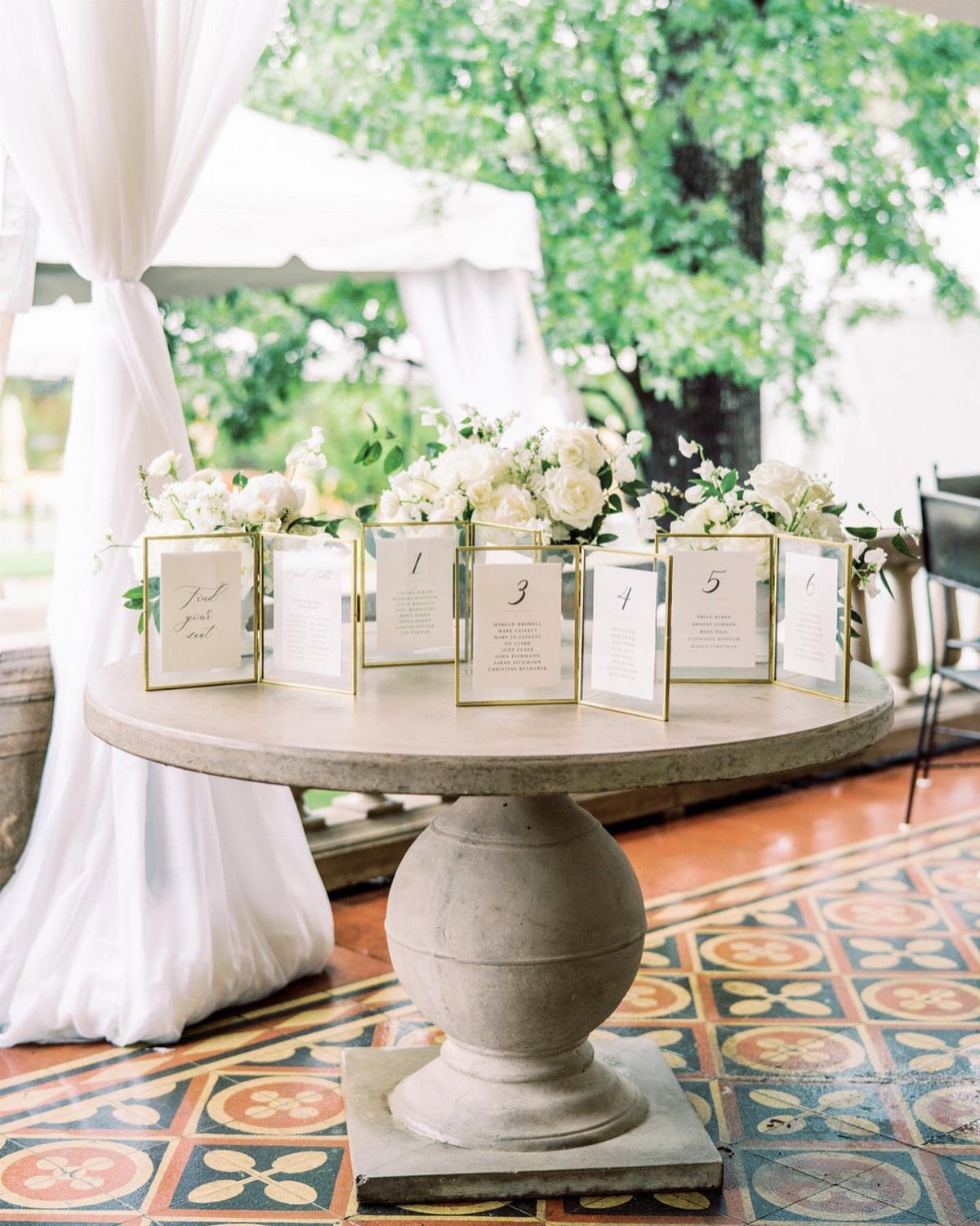 Gold framed seating charts on a stone table with white floral arrangements.