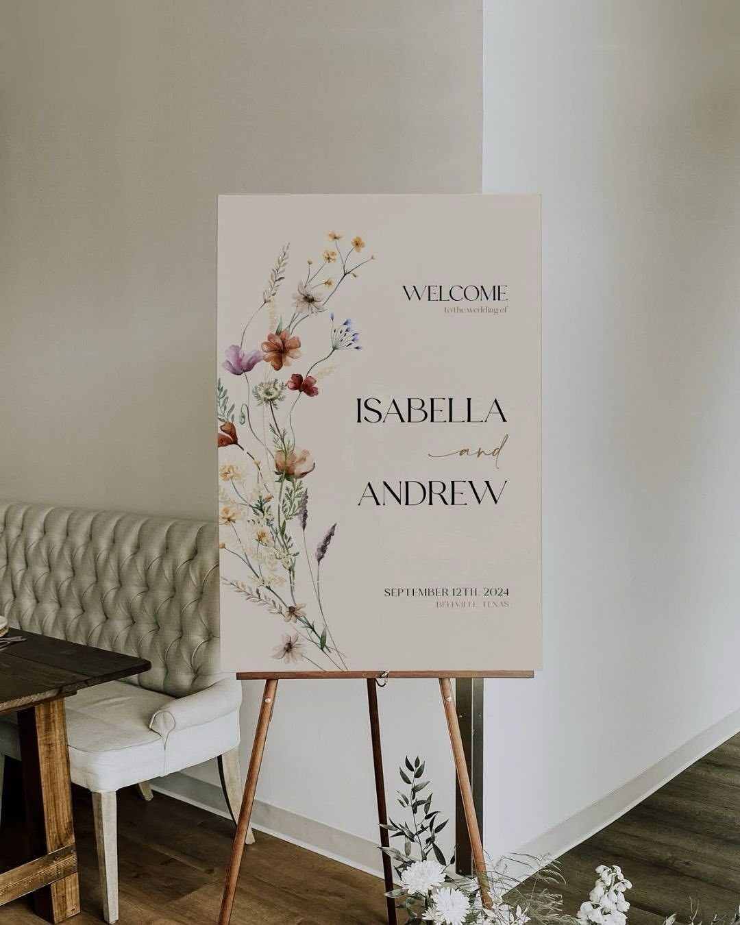 Wedding welcome sign with floral art on a wooden easel in a room.