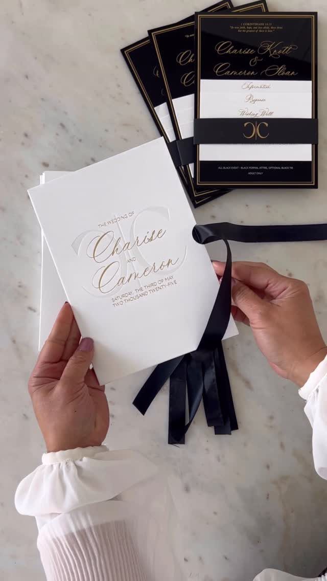 Wedding invitations with gold cursive fonts on white and black cardstock with ribbons