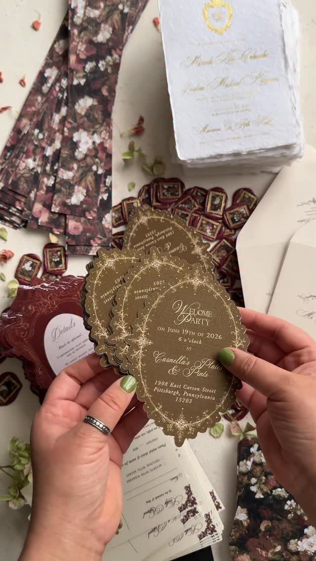 Gold scalloped wedding invitations held by hands amidst floral ribbons and stationery.