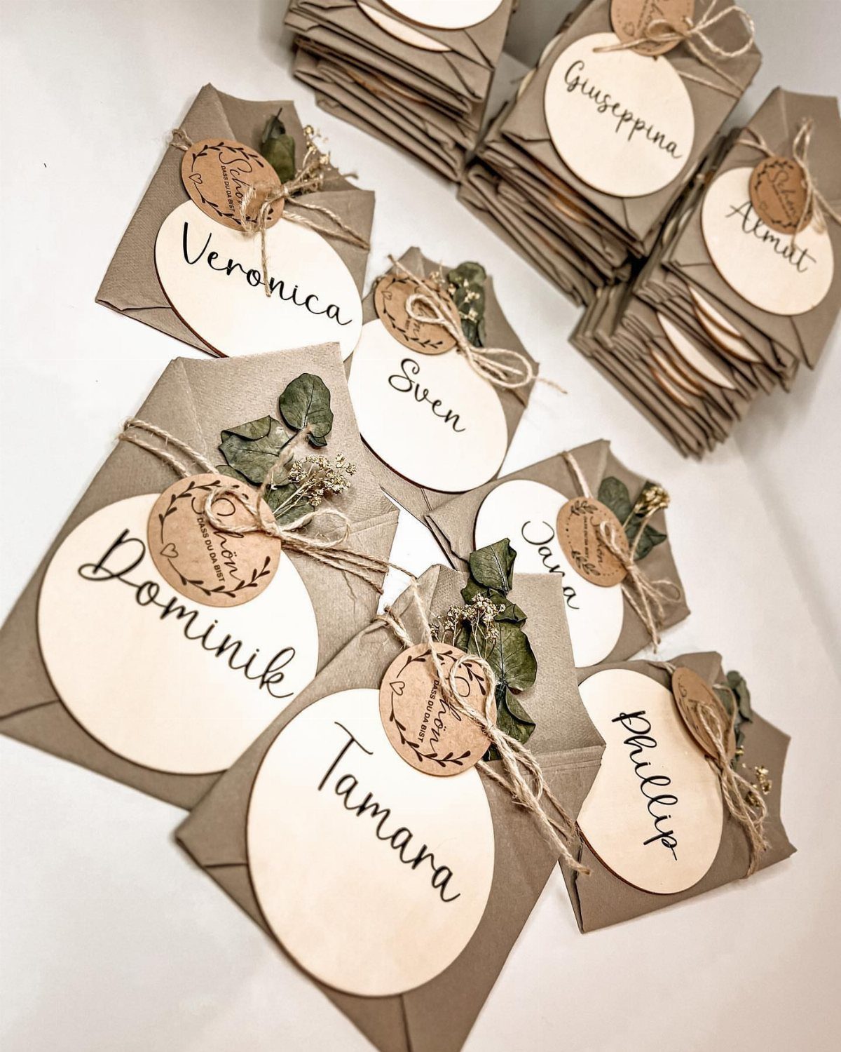 Brown kraft envelopes with white oval name tags tied with twine and greenery.