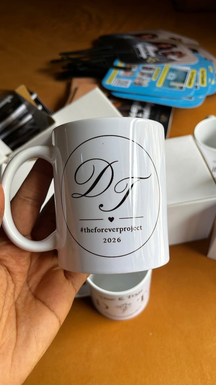 White ceramic mug with custom black logo and hashtag held by a hand.