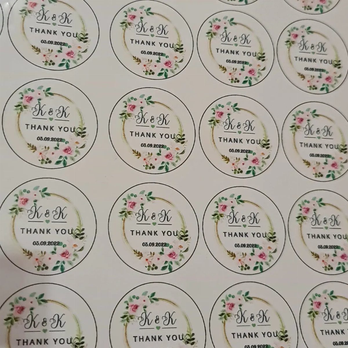 Circular wedding thank you stickers with floral wreaths and initials on a sheet.