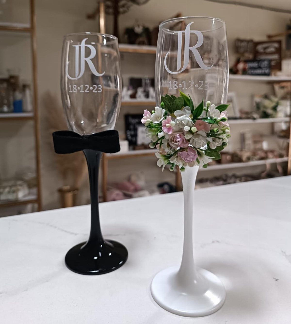 Two personalized champagne flutes with etched initials and date, decorated with a bow and flowers.