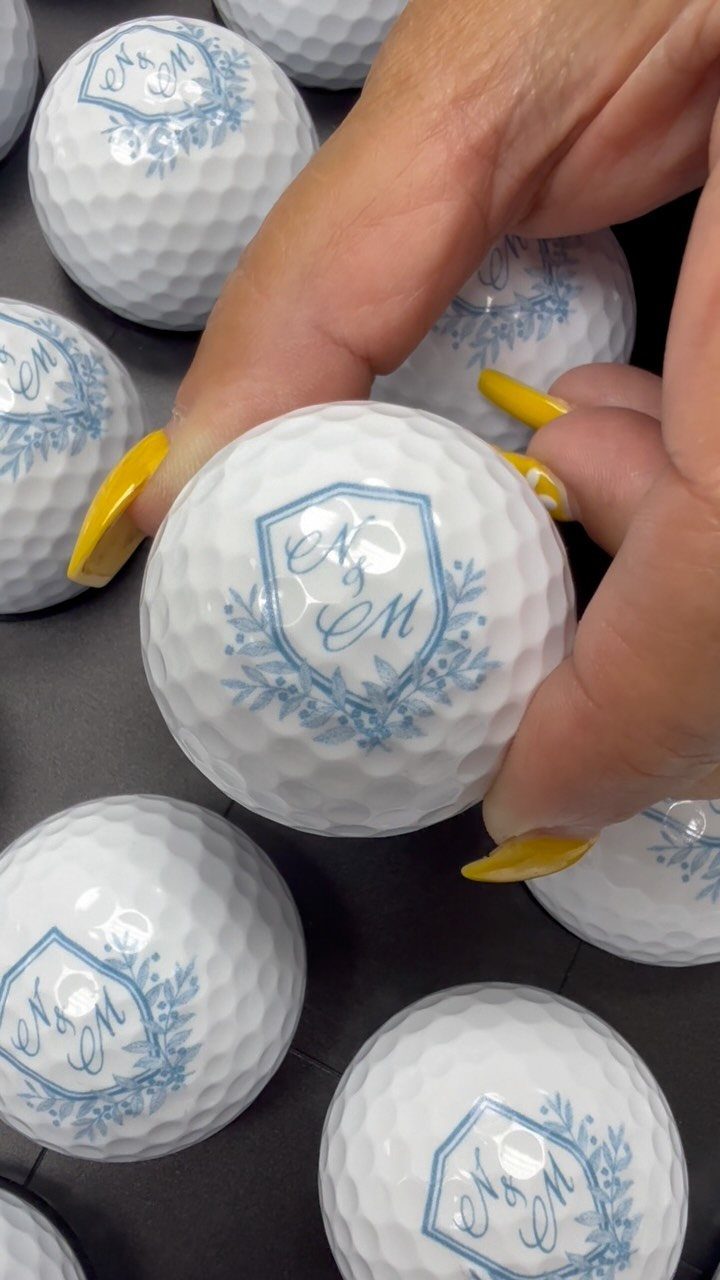 Custom white golf balls with blue crest initials held by a person