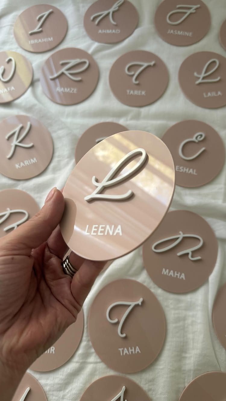 Personalized beige acrylic coasters with white initials and names on white fabric.