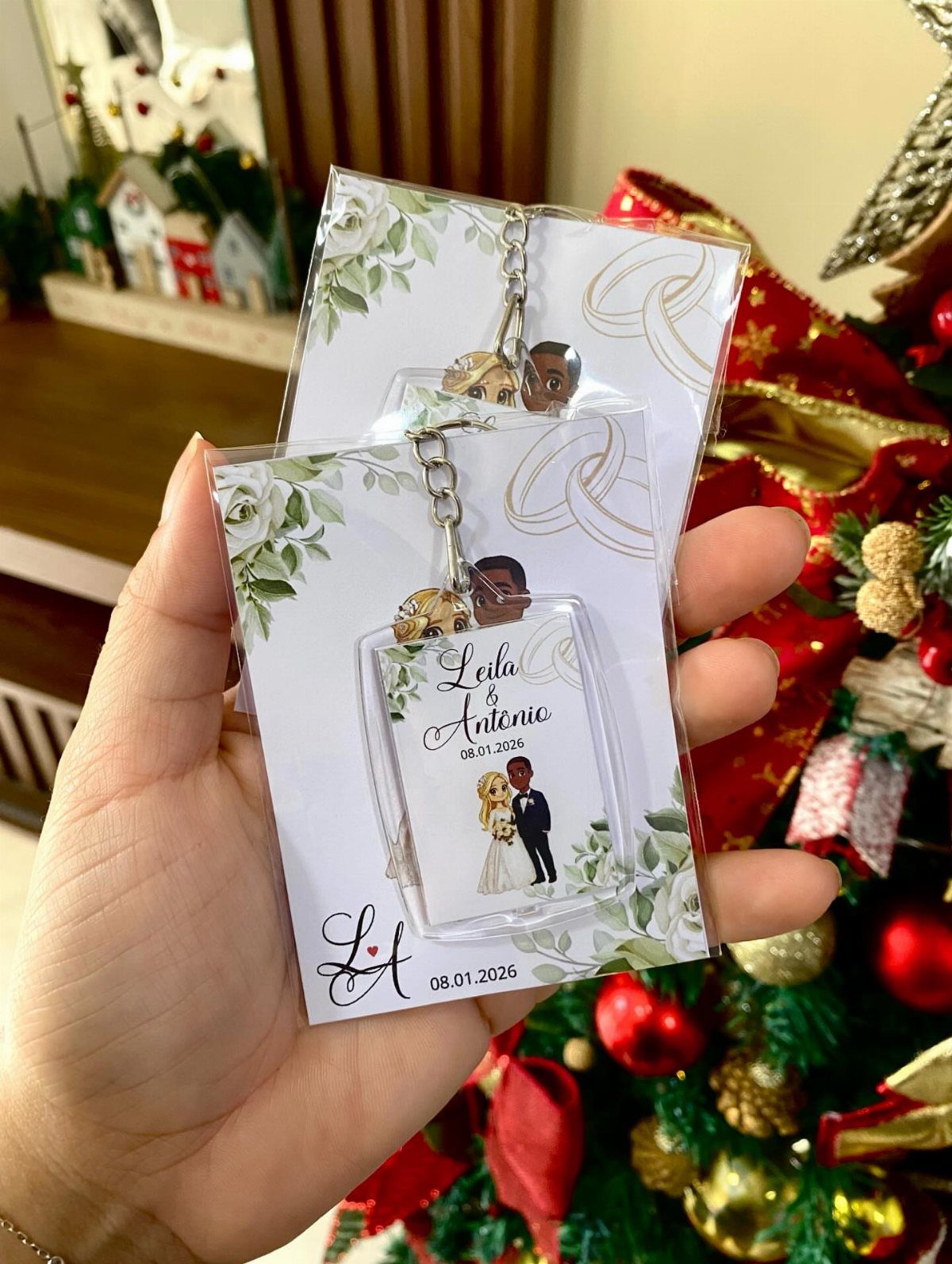 Personalized acrylic wedding keychains with couple illustrations held against a Christmas tree.