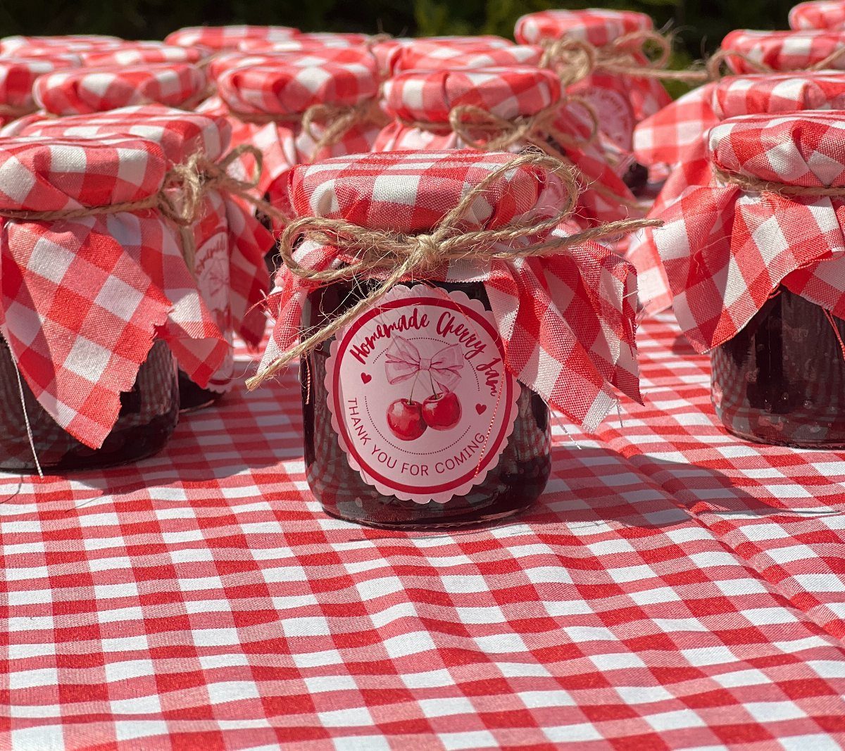 Small jam jars with red checkered lids and thank you labels on tablecloth