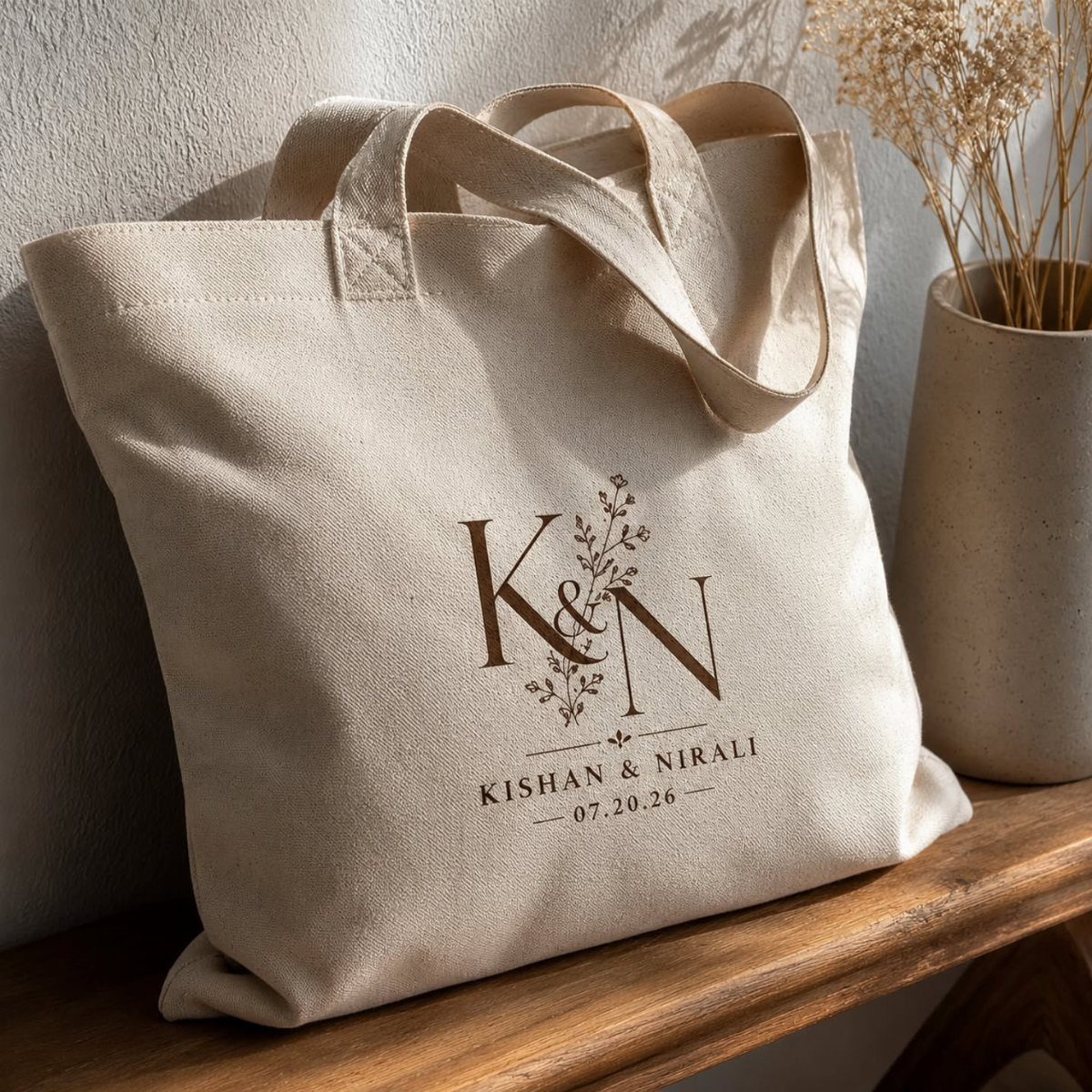 Beige canvas tote bag with personalized wedding initials and names on wooden shelf