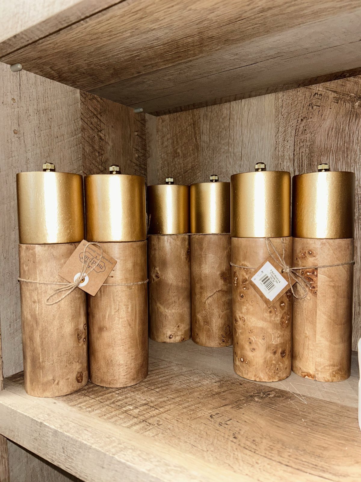 Wooden cylindrical containers with gold lids and twine tags on a rustic shelf