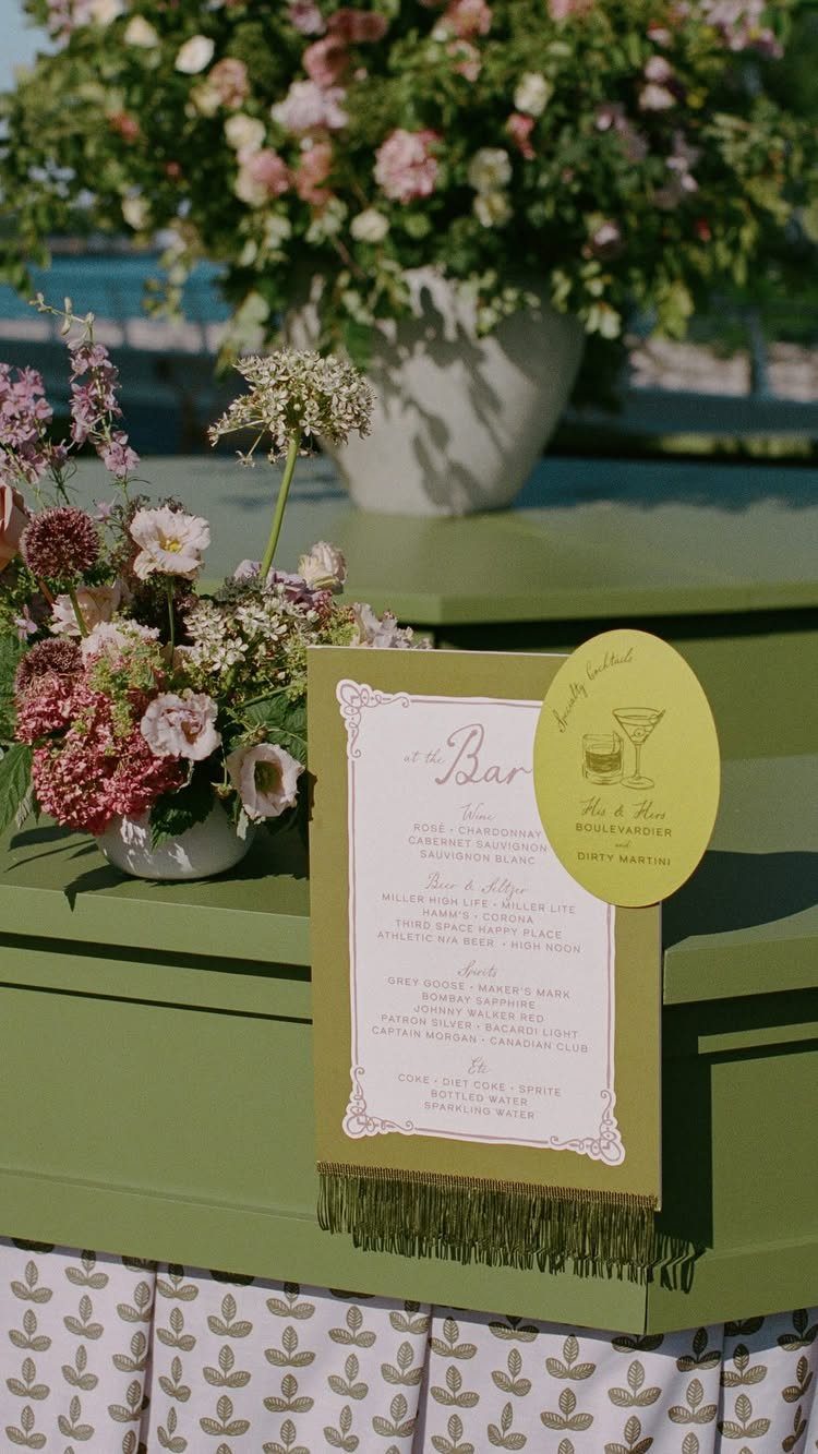 Bar menu card with floral arrangements on a green outdoor table.