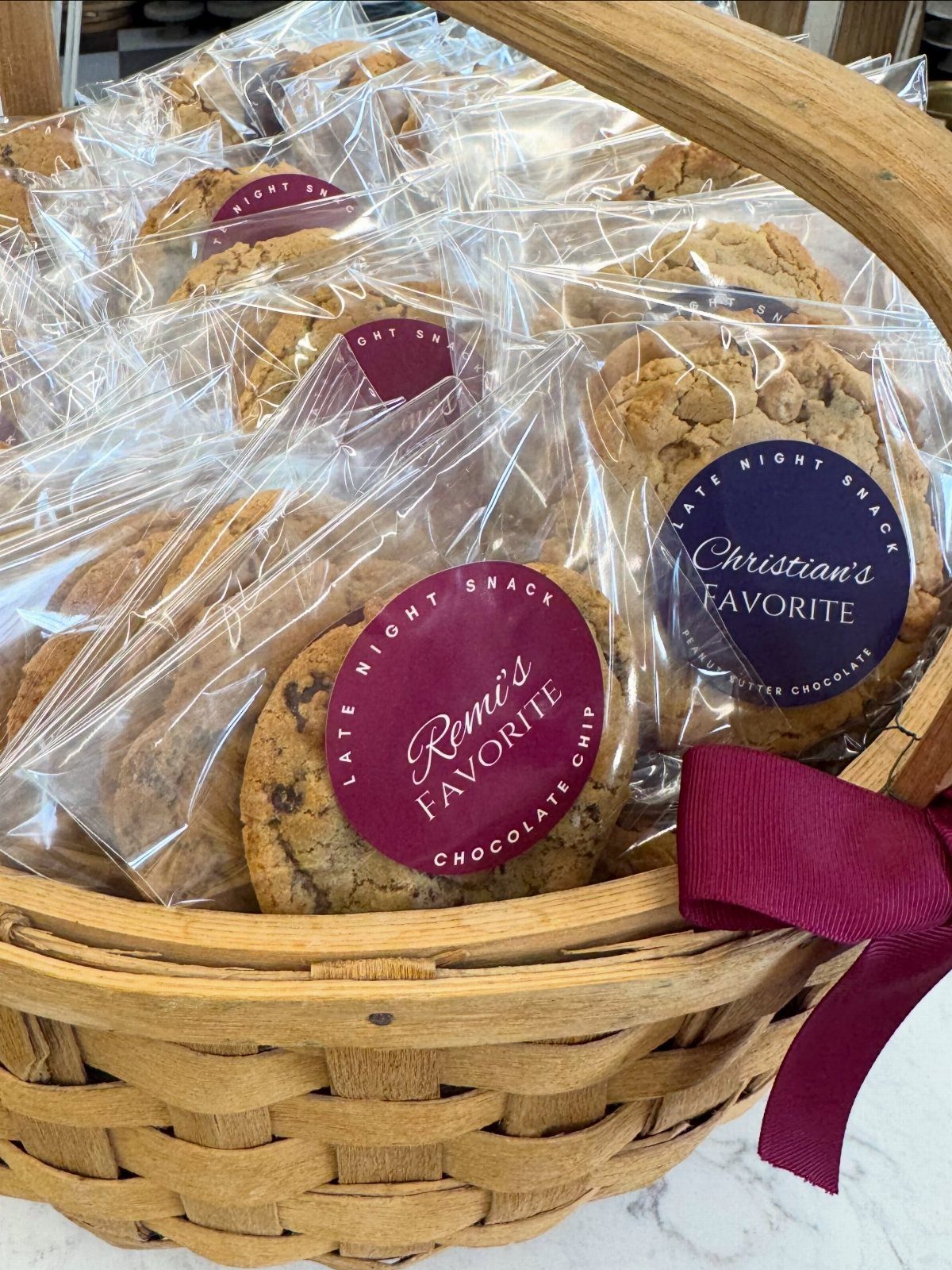 Individually wrapped chocolate chip cookies with custom labels in a wicker basket.