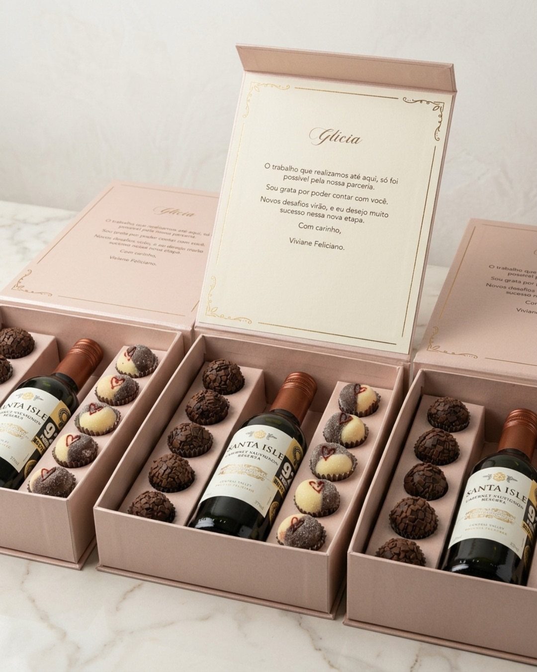 Blush-pink gift boxes containing wine bottles and chocolates with personalized printed notes.