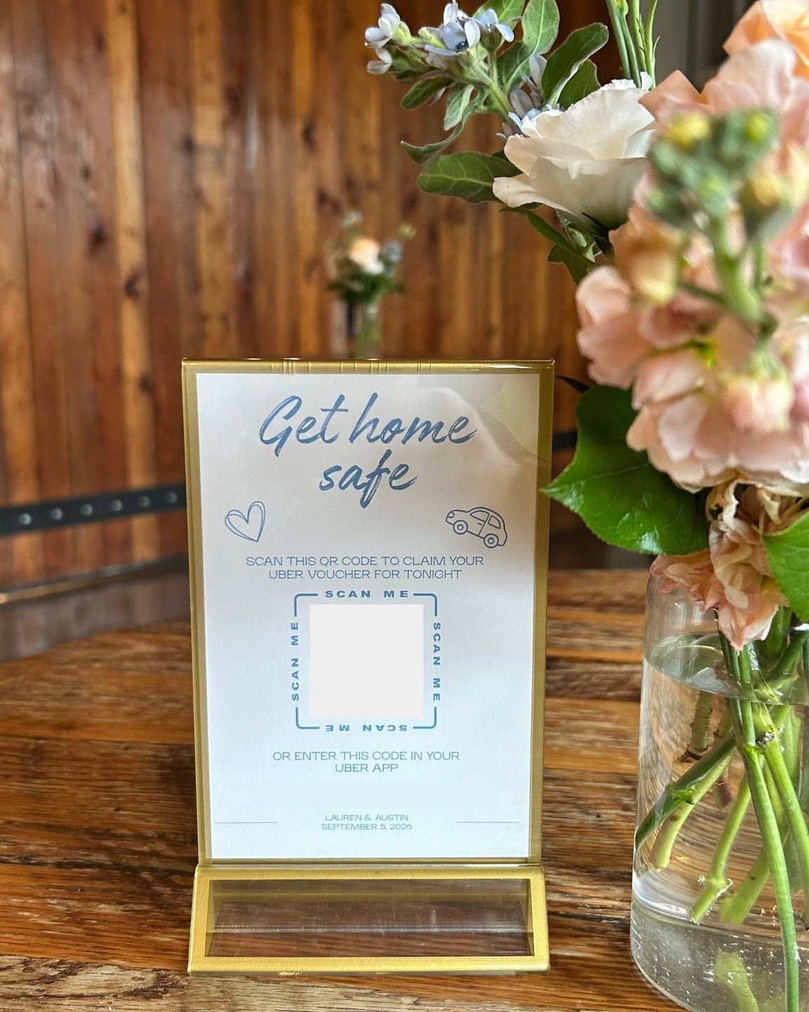 Gold-framed sign with Uber voucher QR code next to peach wedding flowers