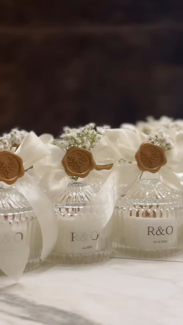 Small glass jars with white ribbons, gold wax seals, and baby's breath flowers.