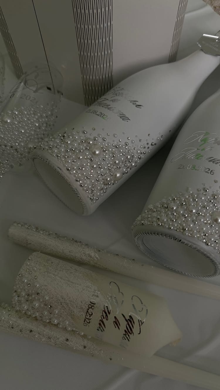 Mini champagne bottles decorated with white pearls and rhinestones on white fabric.