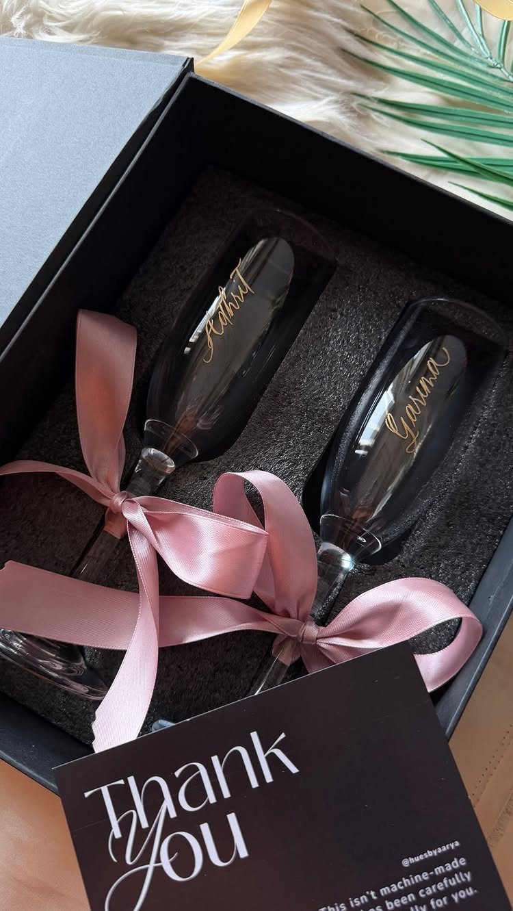 Personalized champagne flutes with gold names in a black gift box with pink ribbon.