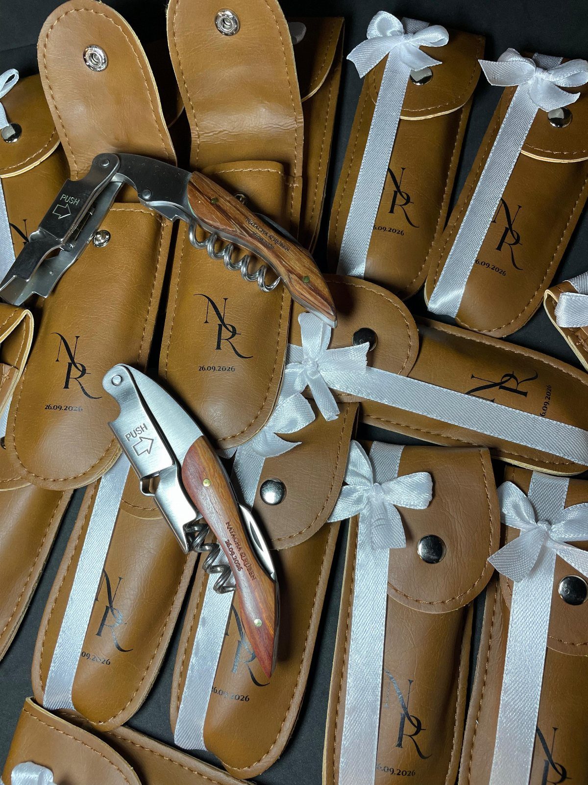 Small wooden and silver corkscrews in brown leather pouches with white satin ribbons.
