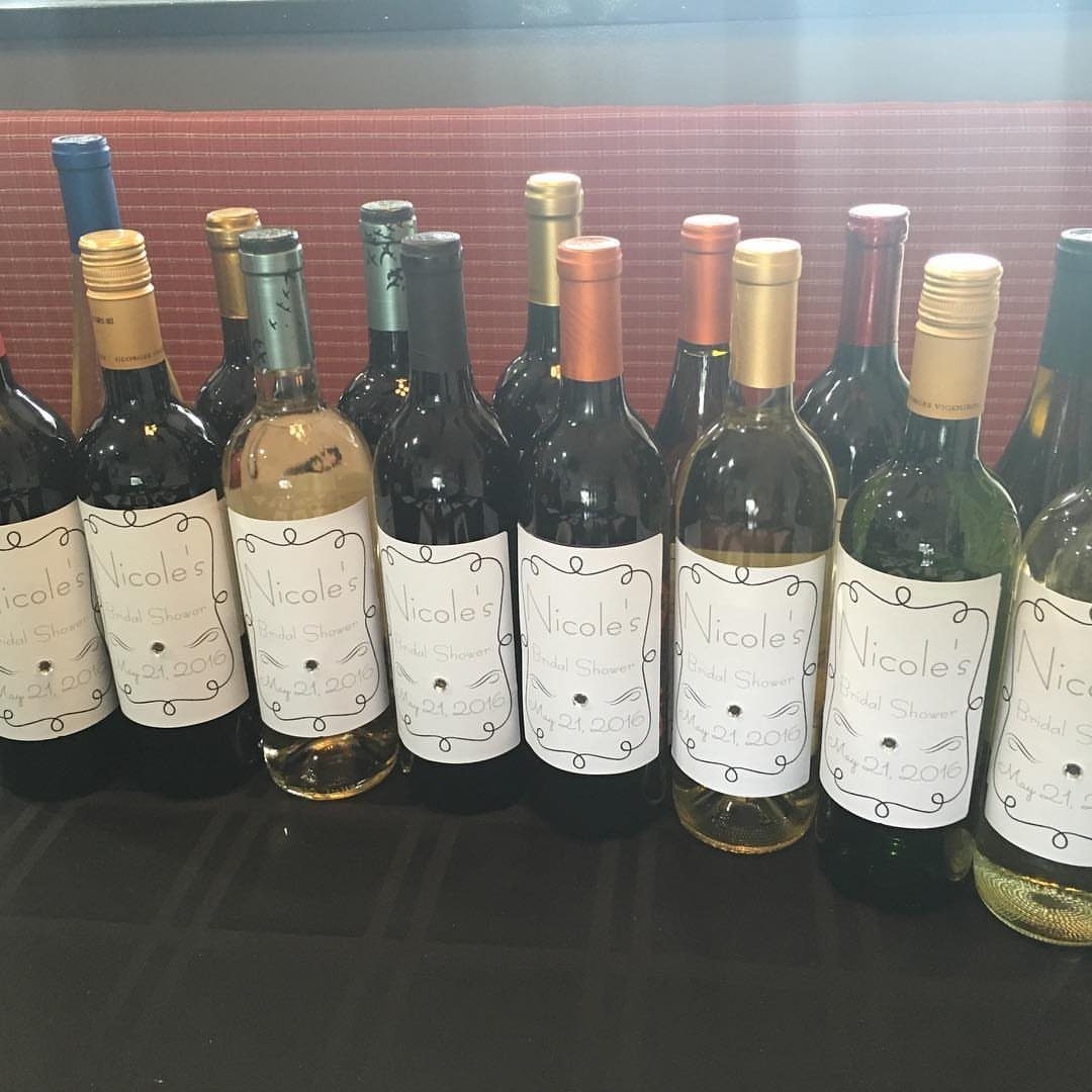 Wine bottles with personalized white labels arranged in a row on a table.